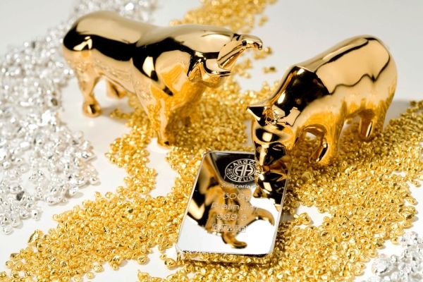 Golden Bull and Bear with Gold Bar Two golden figurines of a bull and a bear standing on piles of gold and silver beads, with a gold bar placed between them.